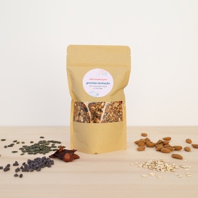 Saco de granola em papel castanho com sementes e frutos secos ao redor