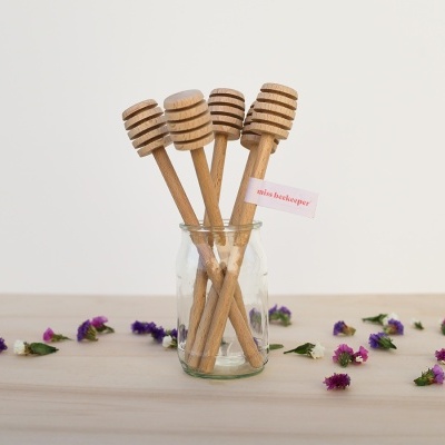 Colheres de mel de madeira em frasco de vidro com flores ao redor