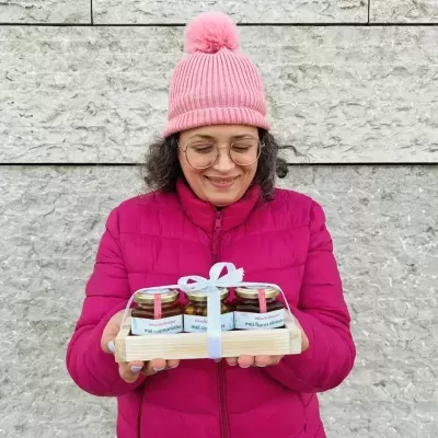 Mulher com casaco e gorro rosa segurando frascos de mel em bandeja de madeira