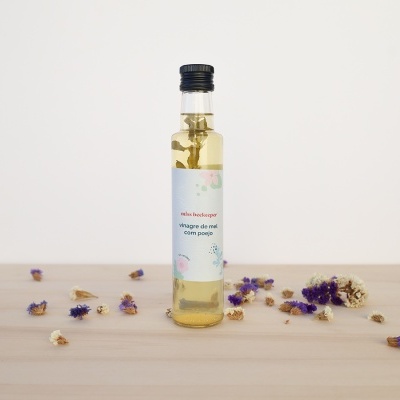 Garrafa de vidro com líquido amarelo e rótulo branco sobre mesa de madeira com flores secas ao redor