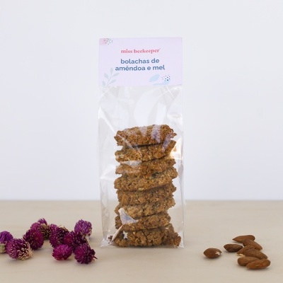 Pacote transparente de bolachas com etiqueta branca e lilás, flores secas roxas e amêndoas