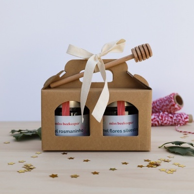 Duas embalagens de mel em caixa castanha com colher de madeira e fita creme