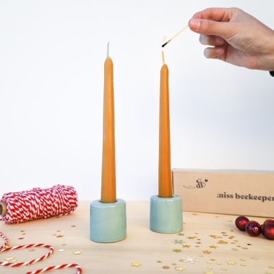 Dois castiçais de cerâmica com velas laranja acesas e articulações para decoração em mesa com caixa e fita