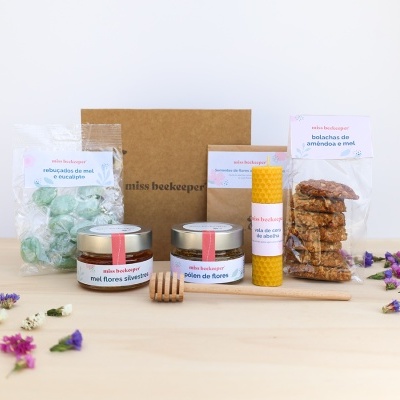 Produtos artesanais de mel e cera de abelha embalados em sacos transparentes e caixa de papelão sobre mesa de madeira clara