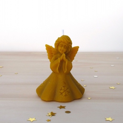 Vela em forma de anjo amarelo mostarda sobre mesa de madeira com confetis dourados e prateados