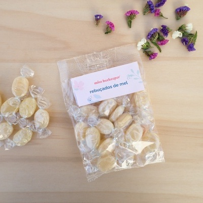 Pacote plástico de rebuçados de mel com rebuçados fora do pacote e flores coloridas ao lado