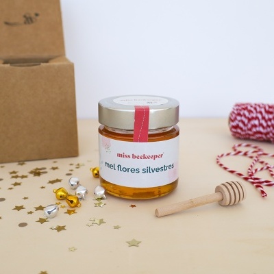 Frasco de mel com etiqueta branca, colher de mel de madeira, linha vermelha e branca e caixa de cartão castanho