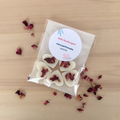 Pacote de velas perfumadas em forma de coração com pétalas de rosa, sobre mesa de madeira clara