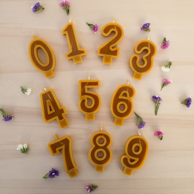Velas em forma de números castanhos com bordas amarelas sobre madeira clara com flores