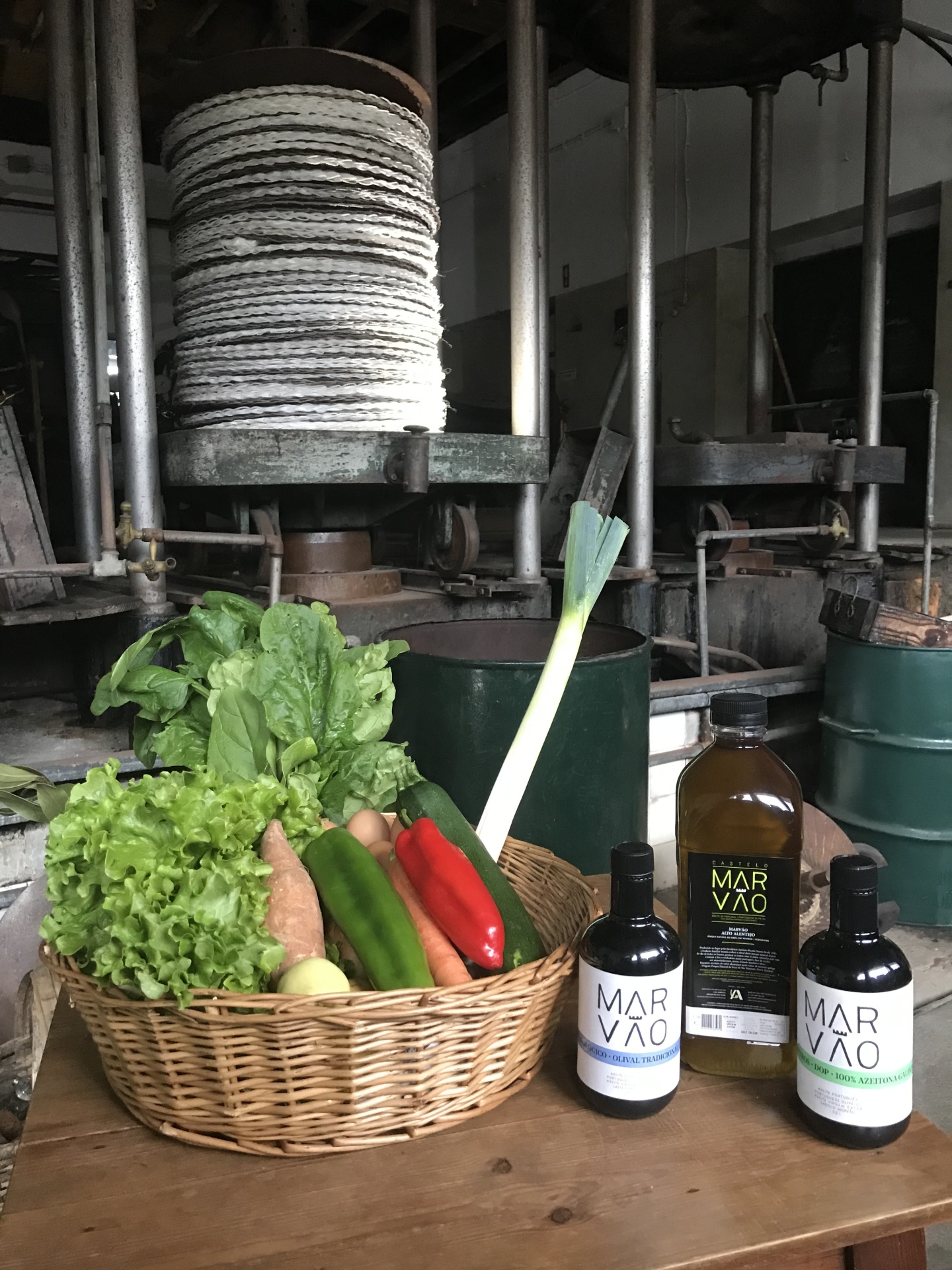Cesto com legumes frescos e garrafas de azeite MAR VÃO sobre mesa de madeira em ambiente industrial