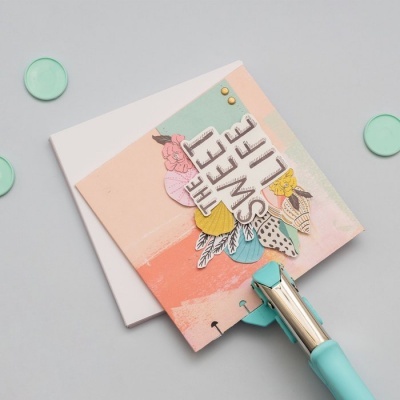 Cartão decorativo com texto THE SWEET LIFE e elementos florais coloridos, sobre envelope branco e abridor de cartas azul-claro.