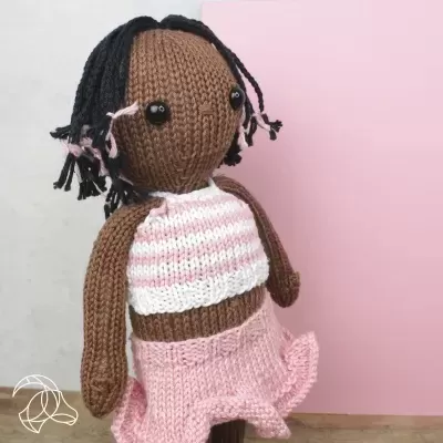 Boneca de malha castanha com roupa rosa e branca, cabelo trançado preto