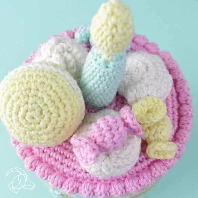 Bolo colorido em crochet com velas e decorações em cores pastel sobre fundo azul