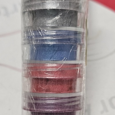 Cinco frascos pequenos com pós coloridos empilhados e embalados em plástico