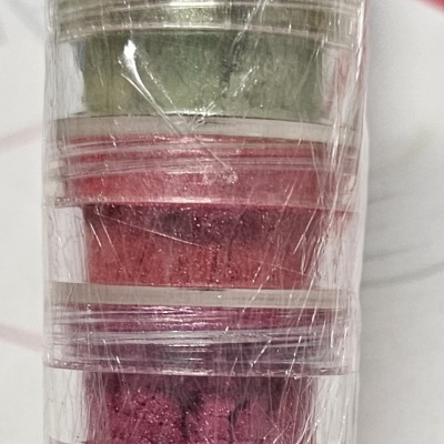 Cinco frascos transparentes com pigmentos coloridos empilhados e enrolados em plástico