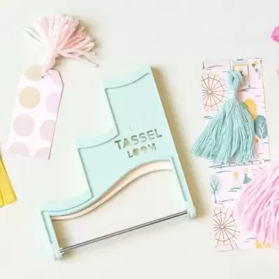 Ferramenta azul direito para borlas com fios coloridos e etiquetas em mesa branca.