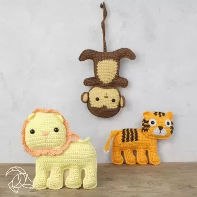 Bonecos amigurumi de croché de leão, macaco e tigre em fundo branco e superfície de madeira.