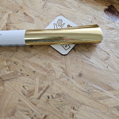 Tubo com tampa dourada metálica e etiqueta com desenho de mão sobre superfície de madeira OSB