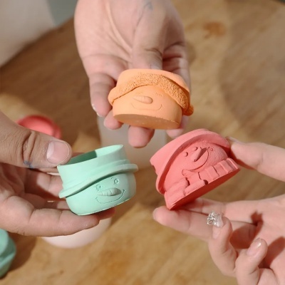 Brinquedos de silicone coloridos com rostos sorridentes nas mãos sobre mesa de madeira