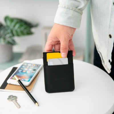 Carteira preta pequena com cartões sobre mesa branca com objetos