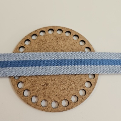 Tira de tecido azul claro e escuro com padrão listrado sobre círculo de cortiça perfurado