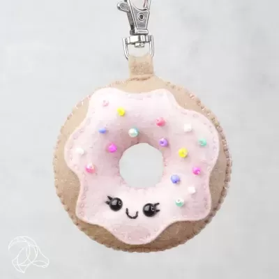 Porta-chaves em forma de donut cor de rosa com rosto sorridente e pompons coloridos