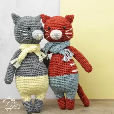 Dois gatos de peluche de crochê coloridos com cachecóis, sobre mesa de madeira
