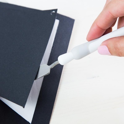 Mão com bisturi cortando papel preto sobre superfície branca