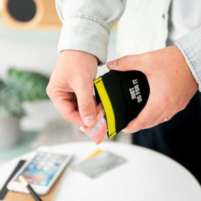 Carteira preta com detalhe amarelo e texto, mãos segurando dinheiro e carteira