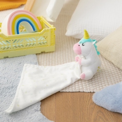 Unicórnio de peluche branco com chifre amarelo segurando pano branco em tapete