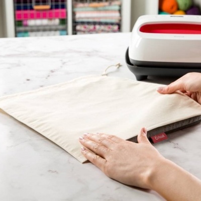 Saco de tecido branco com cordão e máquina branca e vermelha ao fundo numa mesa.