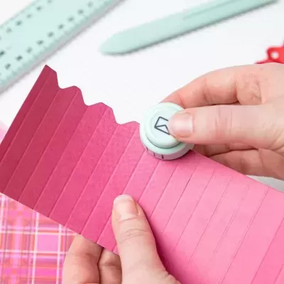 Mãos a usar ferramenta branca para marcar papel rosa com textura ondulada