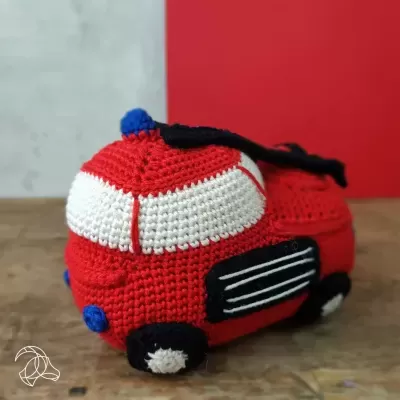 Carro de brinquedo em croché vermelho, branco, preto e azul sobre mesa de madeira