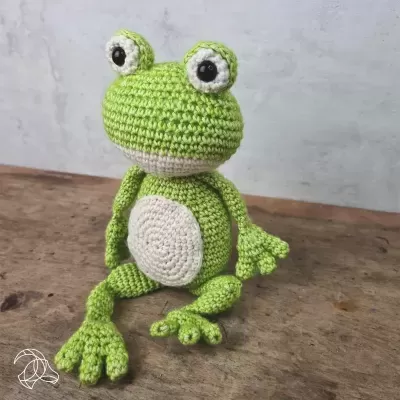 Boneco de rã em croché sentado numa superfície de madeira