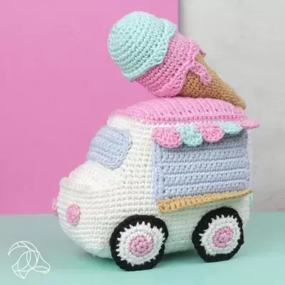 Brinquedo de camião de gelados em crochet com gelado no topo, fundo rosa e cinza.