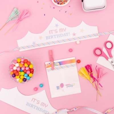 Coroa de aniversário branca e colorida com doces, tesouras e decorações sobre fundo rosa