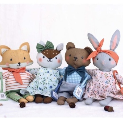 Quatro bonecos de pelúcia animais com roupas coloridas sentados em fundo branco