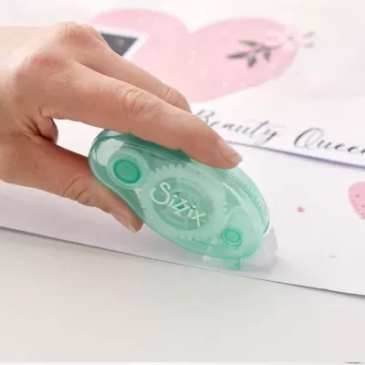 Cola de fita adesiva transparente Sizzix com corpo verde translúcido a ser usada em papel decorativo com corações.