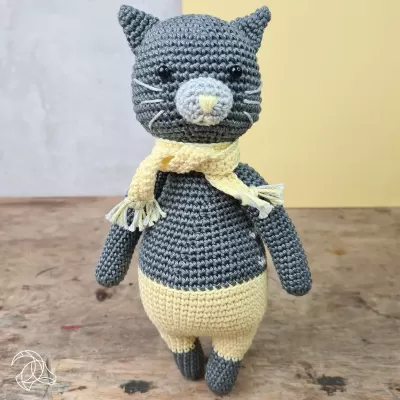 Boneco de gato de crochê cinzento com cachecol amarelo sobre madeira