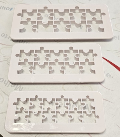 Três moldes de plástico branco com formato de peças de puzzle sobre superfície branca