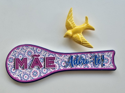 Colher decorativa com padrão colorido e texto 'MÃE Adoro-te!' ao lado de figura amarela de pássaro.