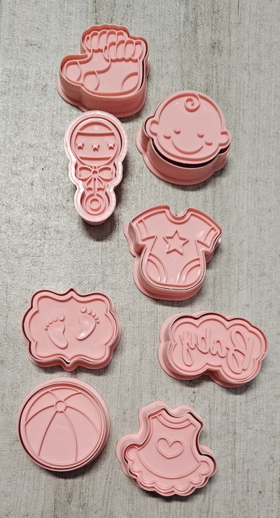Cortadores de biscoito rosa com formas de bebé em superfície cinza