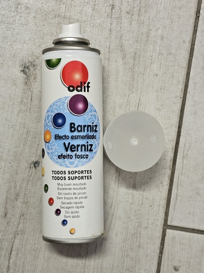 Lata de verniz em spray branca com tampa transparente ao lado num fundo de madeira clara