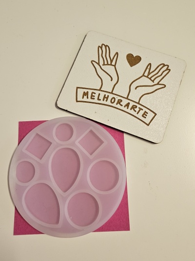 Molde de silicone transparente e cartão branco com ilustração de mãos e texto MELHORARTE