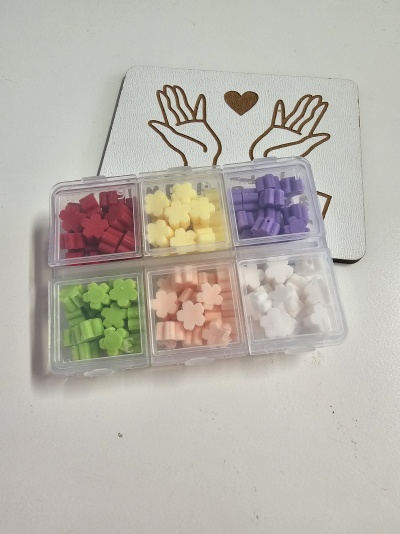 Caixa plástica com pequenos objetos florais coloridos sobre cartão com ilustração de mãos e coração