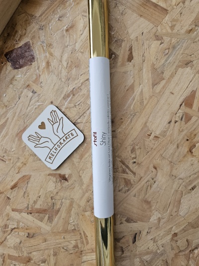 Rolo de papel autocolante dourado brilhante com etiqueta branca e etiqueta MELHOMARTE sobre madeira