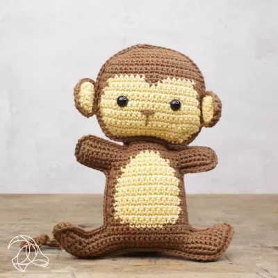 Boneco de macaco em crochet castanho e bege sentado sobre madeira