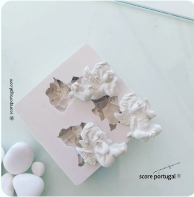 Três anjos brancos em gesso, pedras brancas e molde sobre superfície clara