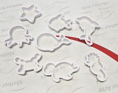 Moldes brancos para bolachas em várias formas sobre superfície branca com faixa vermelha