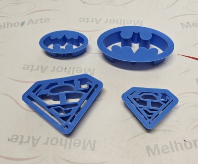 Cortadores de biscoito azul com símbolos de Batman e Superman sobre papel branco